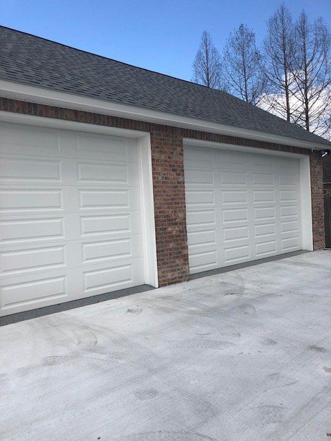 A garage with three white garage doors and a brick wall.