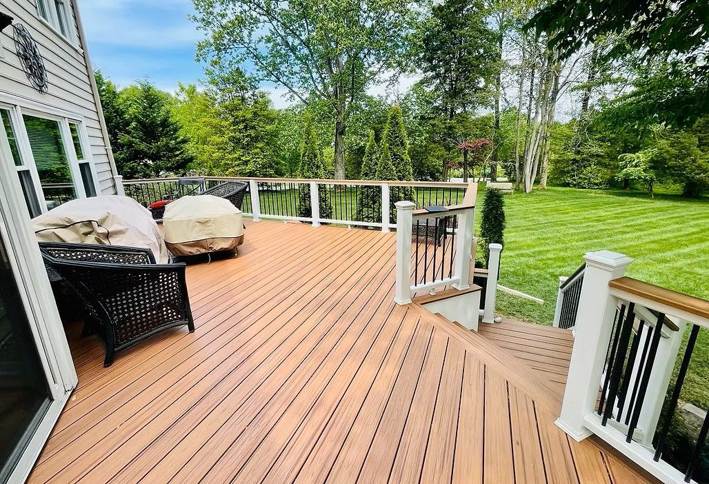 Wooden deck with outdoor furniture, overlooking a grassy yard with trees.