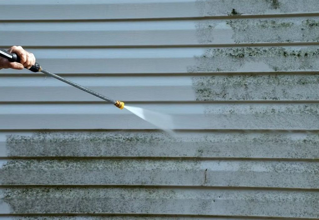 Power washer spraying a dirty, algae-covered siding, cleaning a portion of the wall.