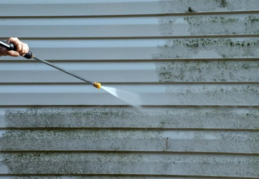 Power washer spraying a dirty, algae-covered siding, cleaning a portion of the wall.
