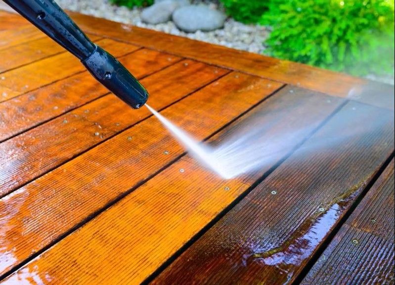 Pressure washer cleaning a wooden deck, removing dirt and revealing fresh wood.