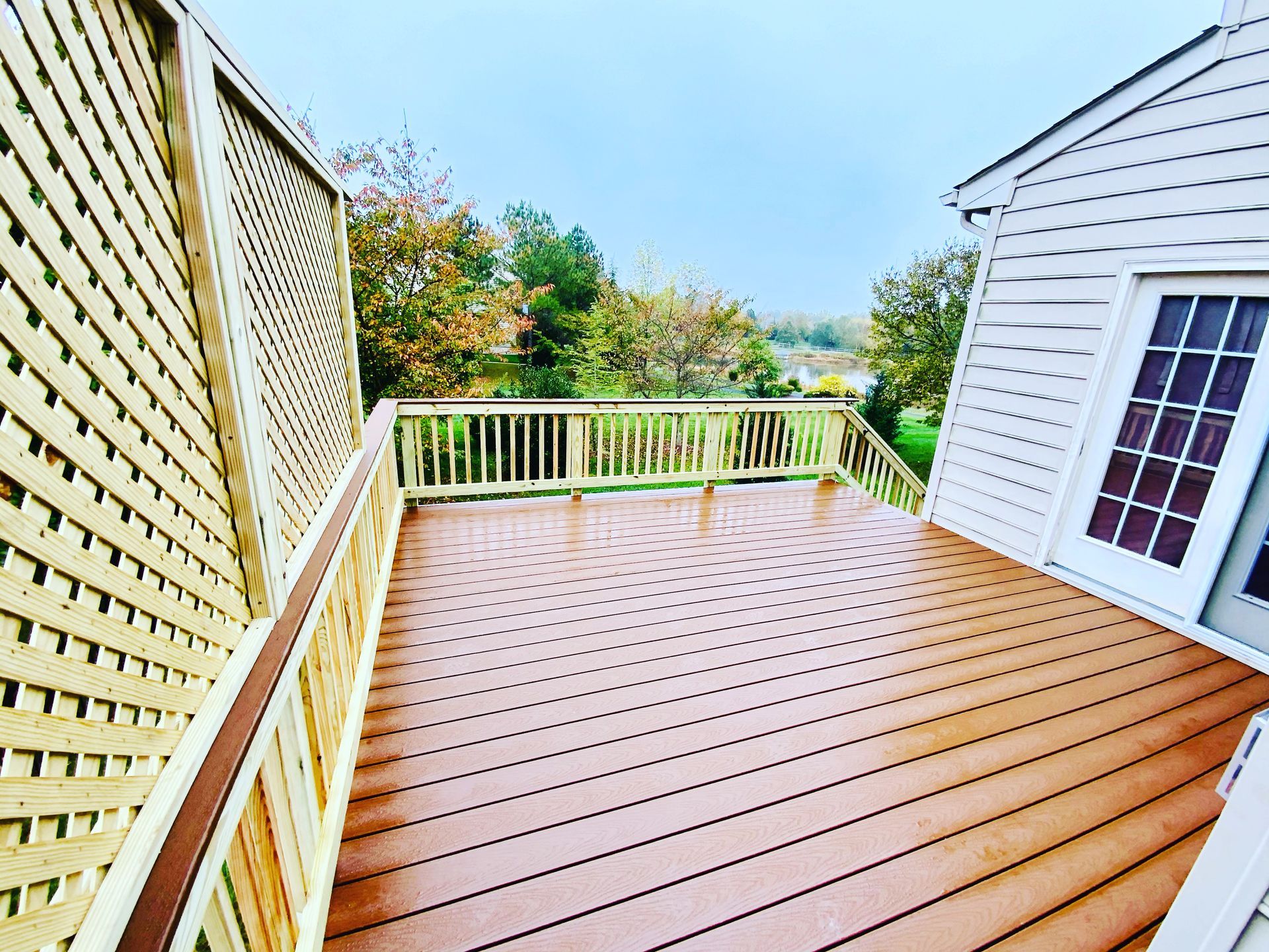 Wooden deck with lattice and railing, overlooking trees and a green lawn.