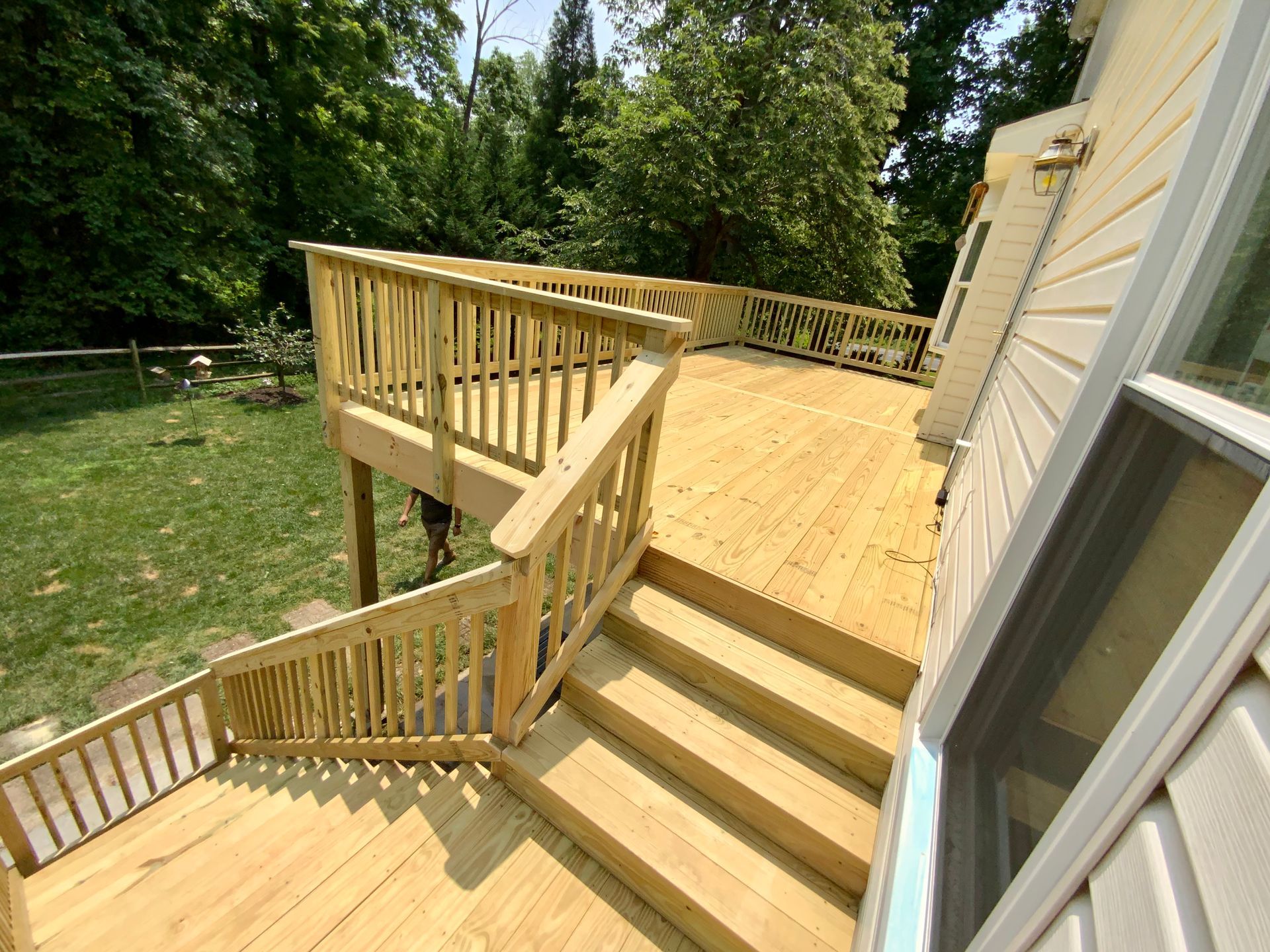 Wooden deck with steps, railings, and a view of a grassy yard with trees.