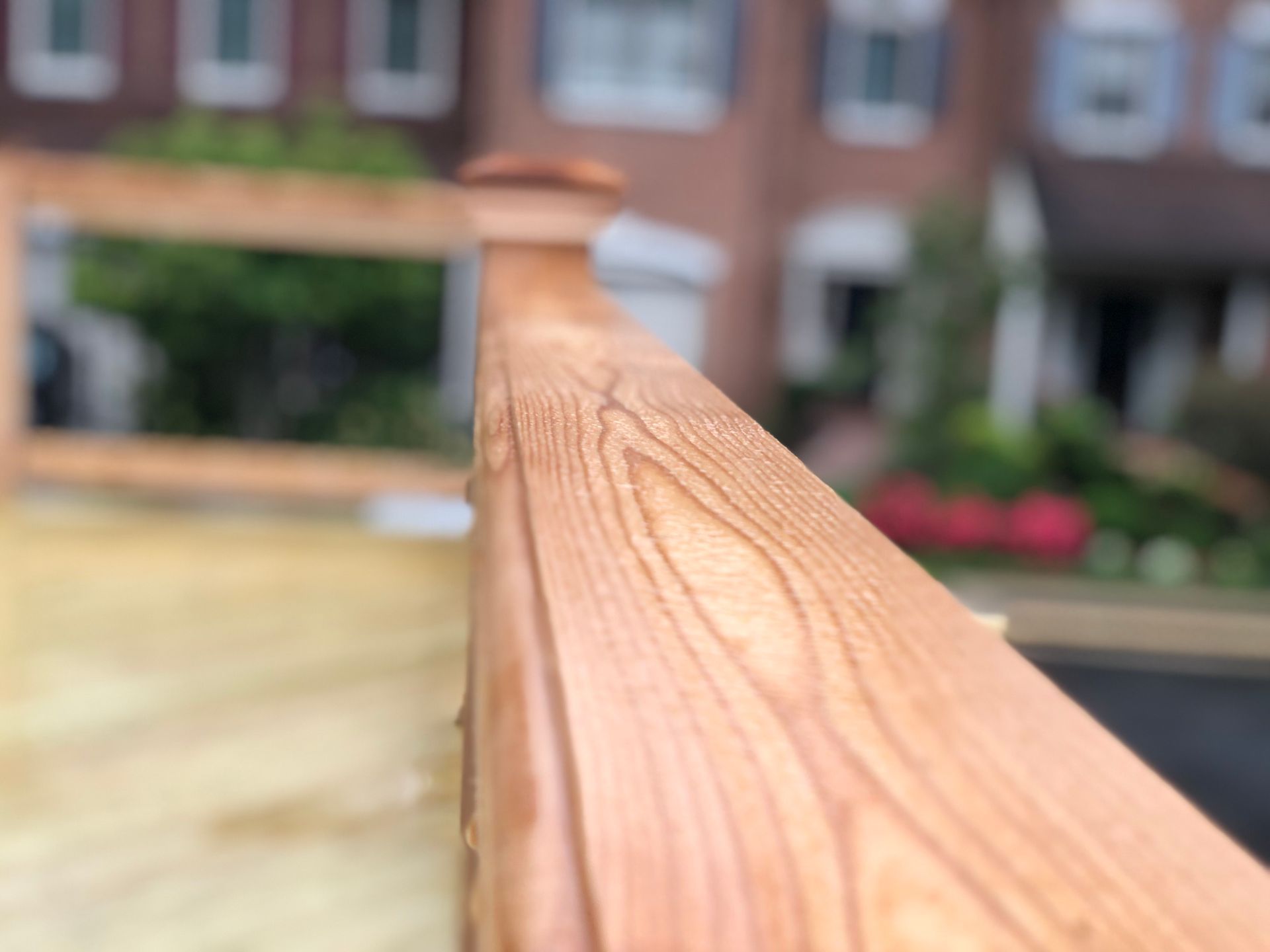 Close-up of a wooden railing with a blurred background of a house and greenery.