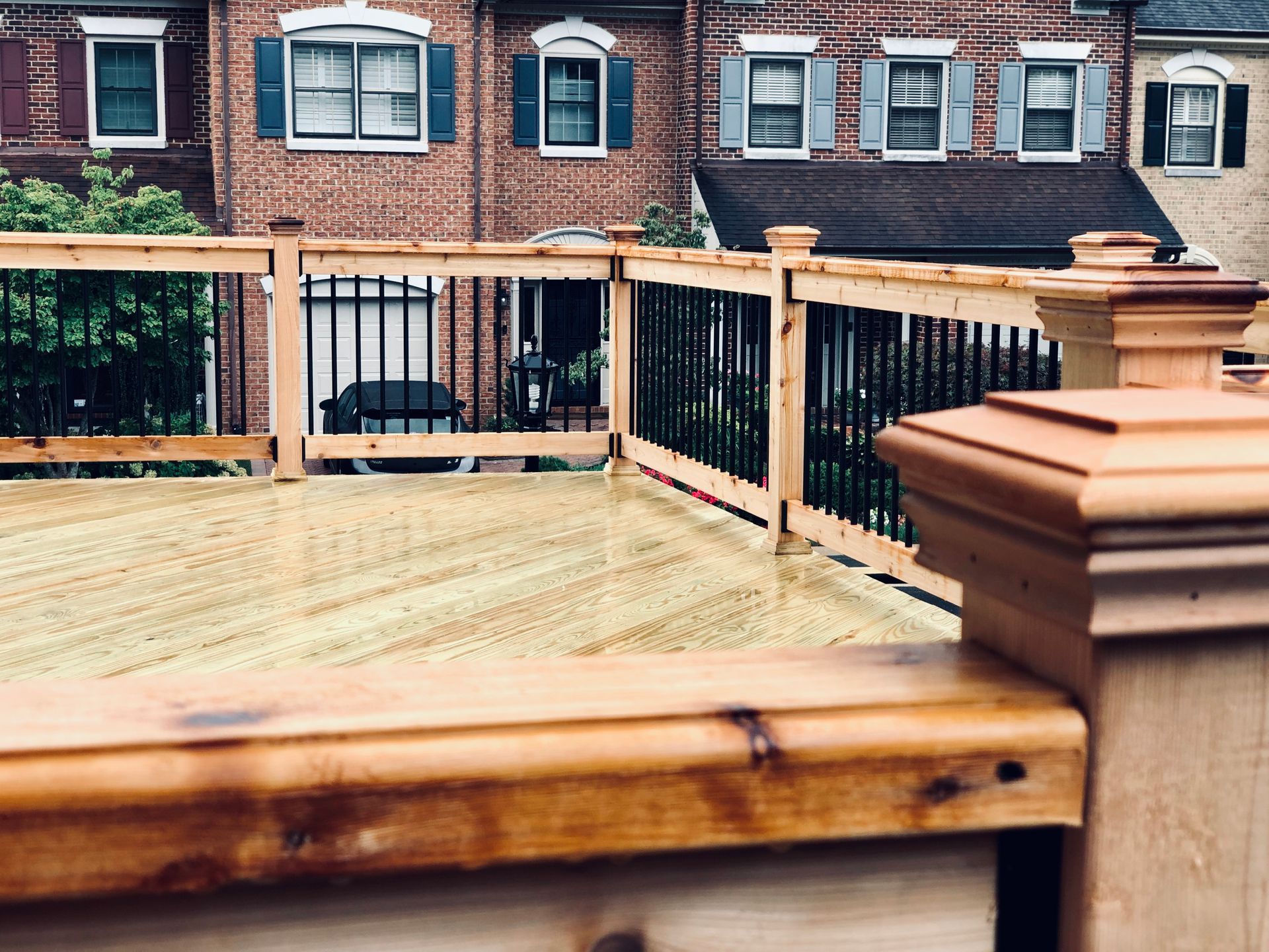 Wooden deck with black railings and a brick building backdrop.