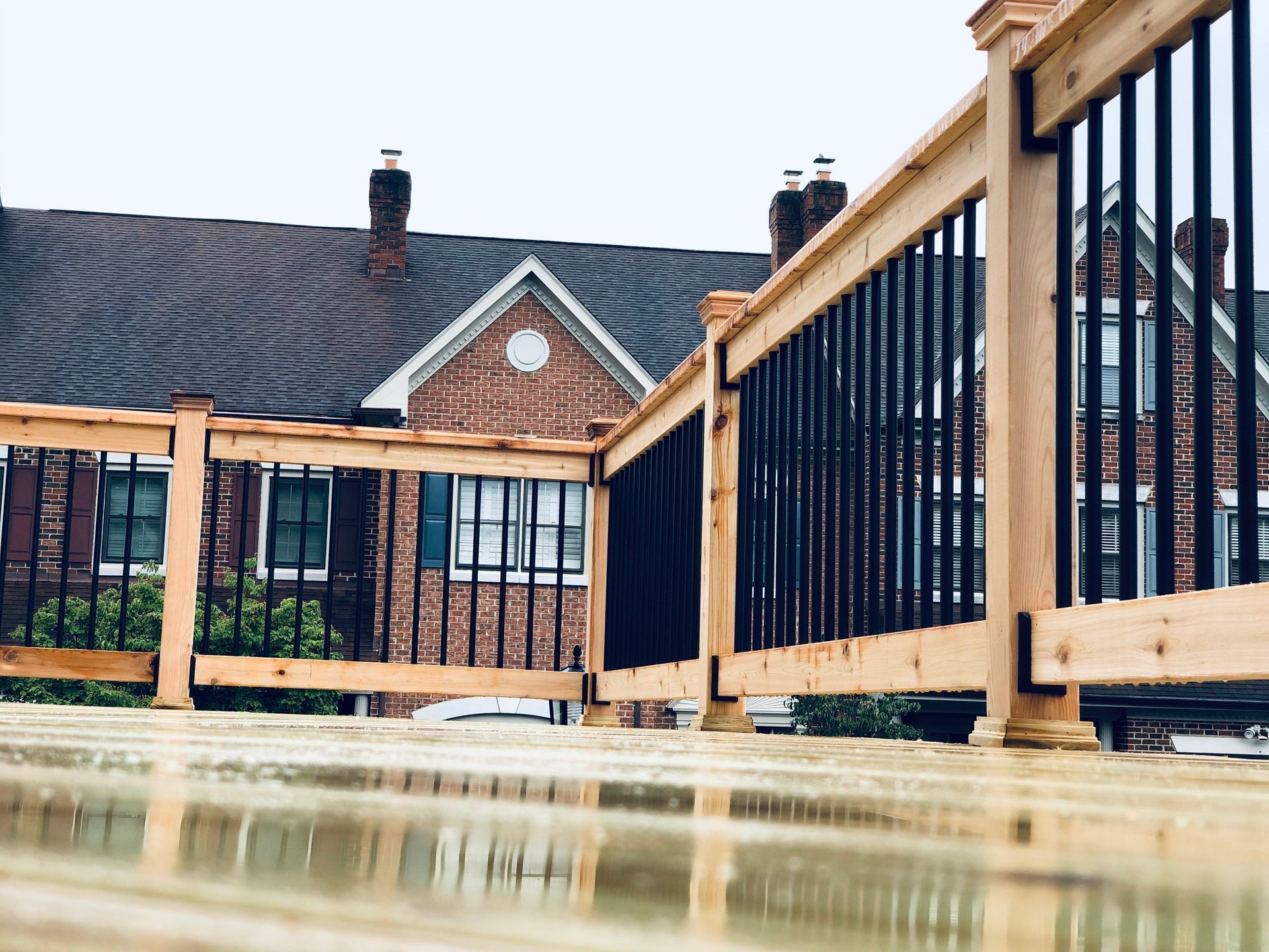 Wooden deck with black railing overlooking a brick house with a dark roof.