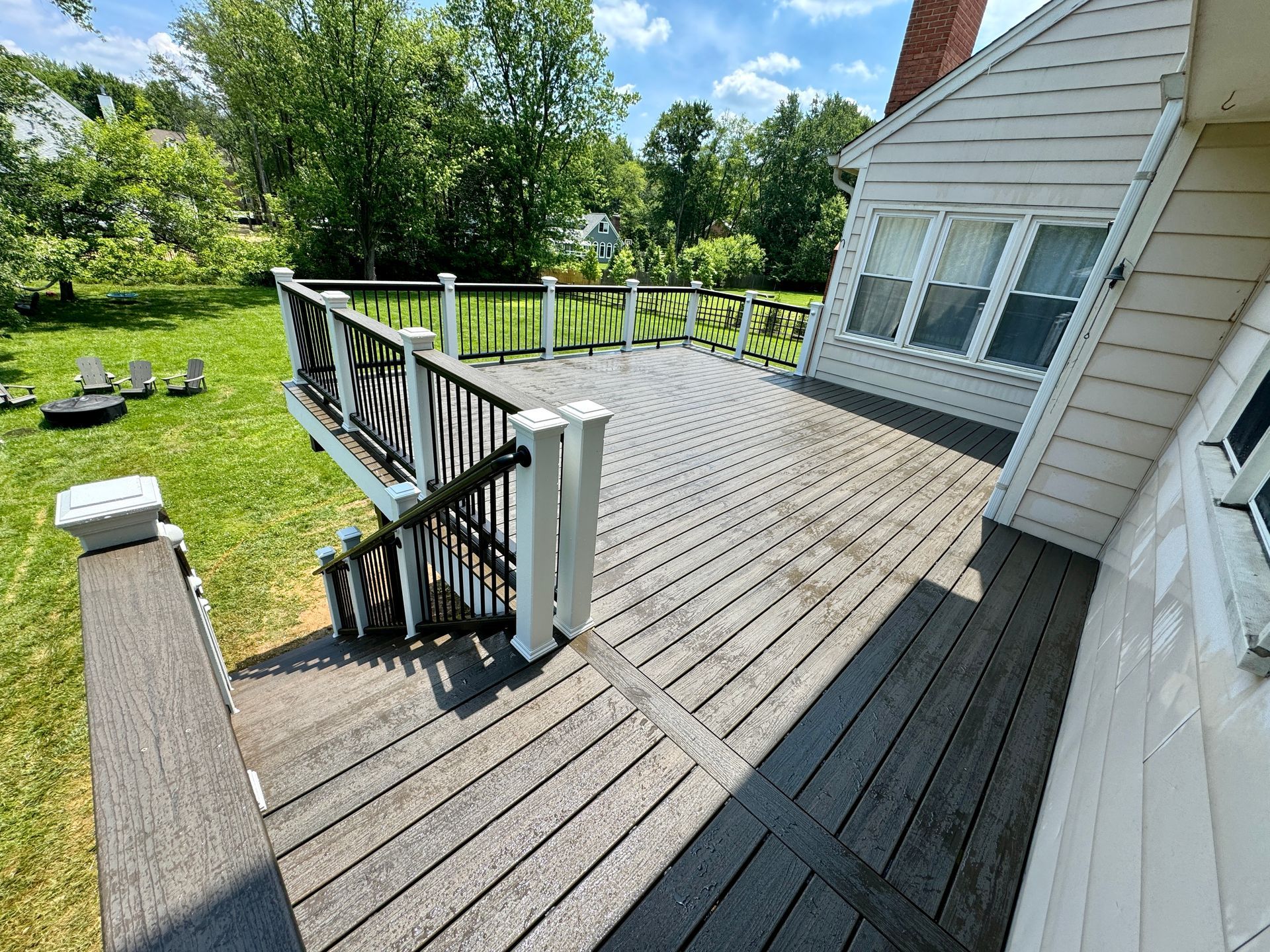 A composite deck with black railing and white posts is adjacent to a white house, on a sunny day.
