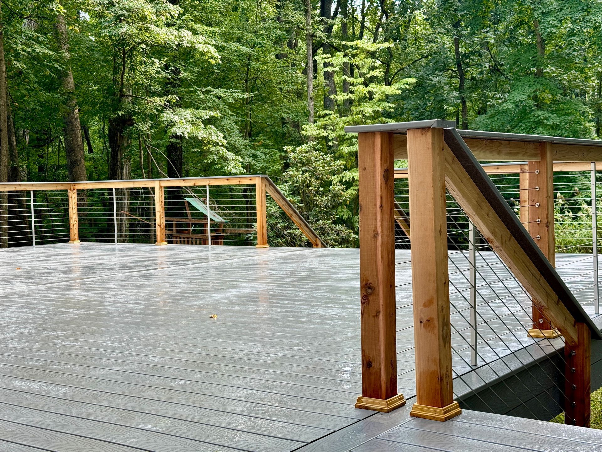 Wooden deck with cable railings overlooks a forest.
