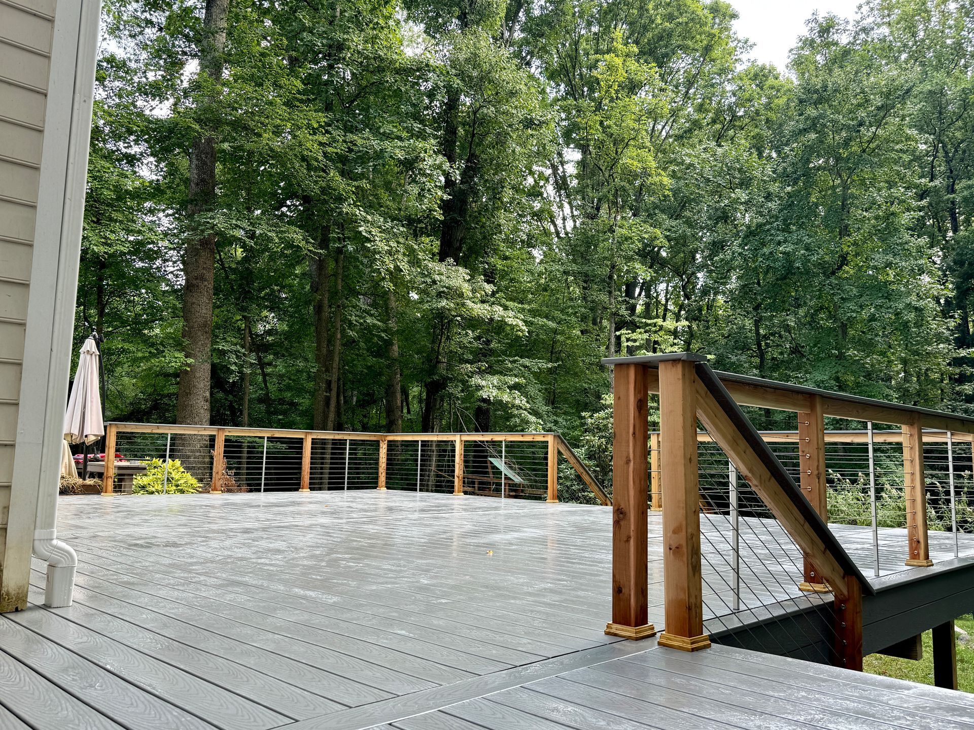 Gray deck with wooden railing and cable infill overlooking trees.