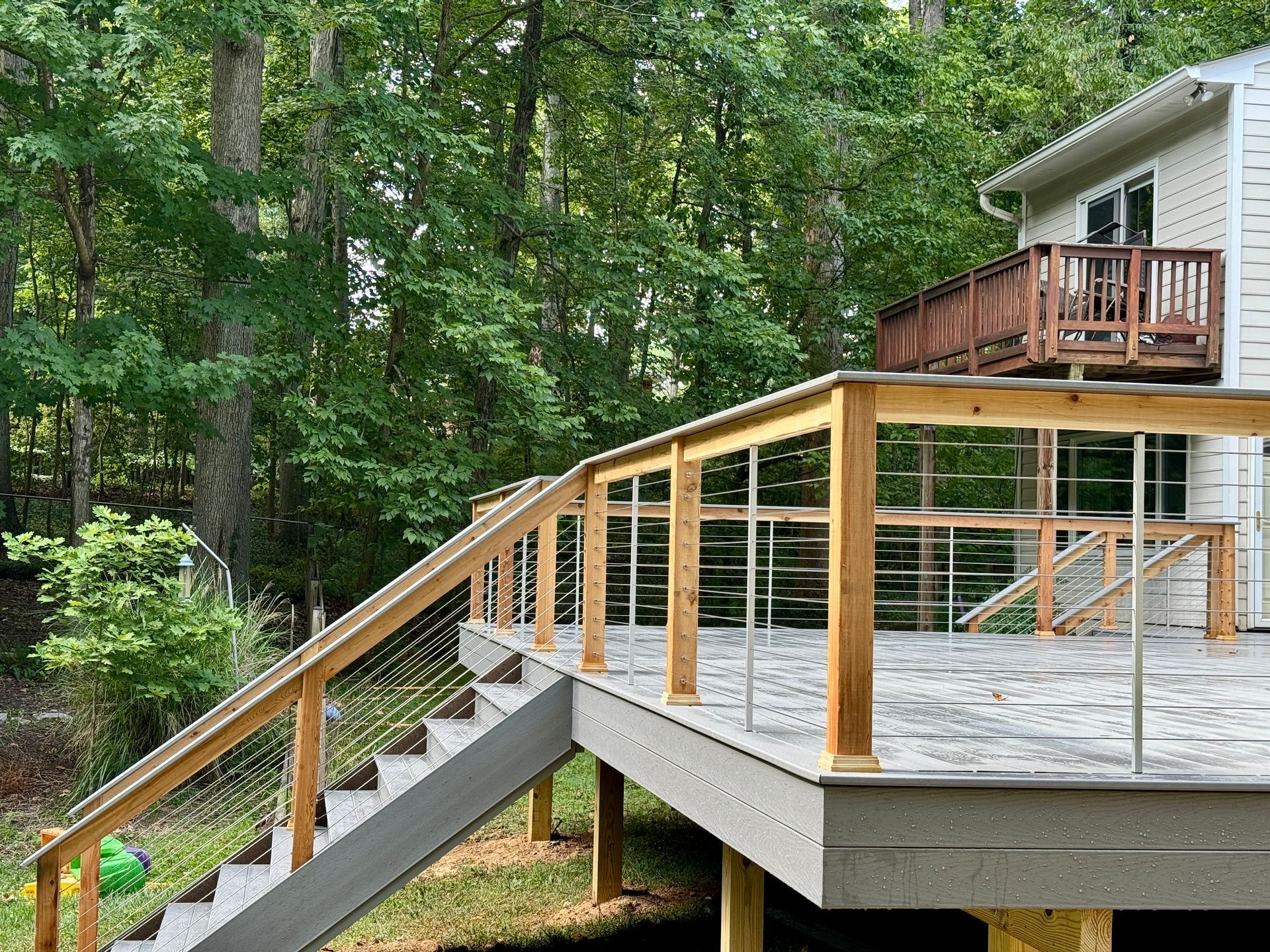 Wooden deck with stairs, cable railing, and a view of trees.