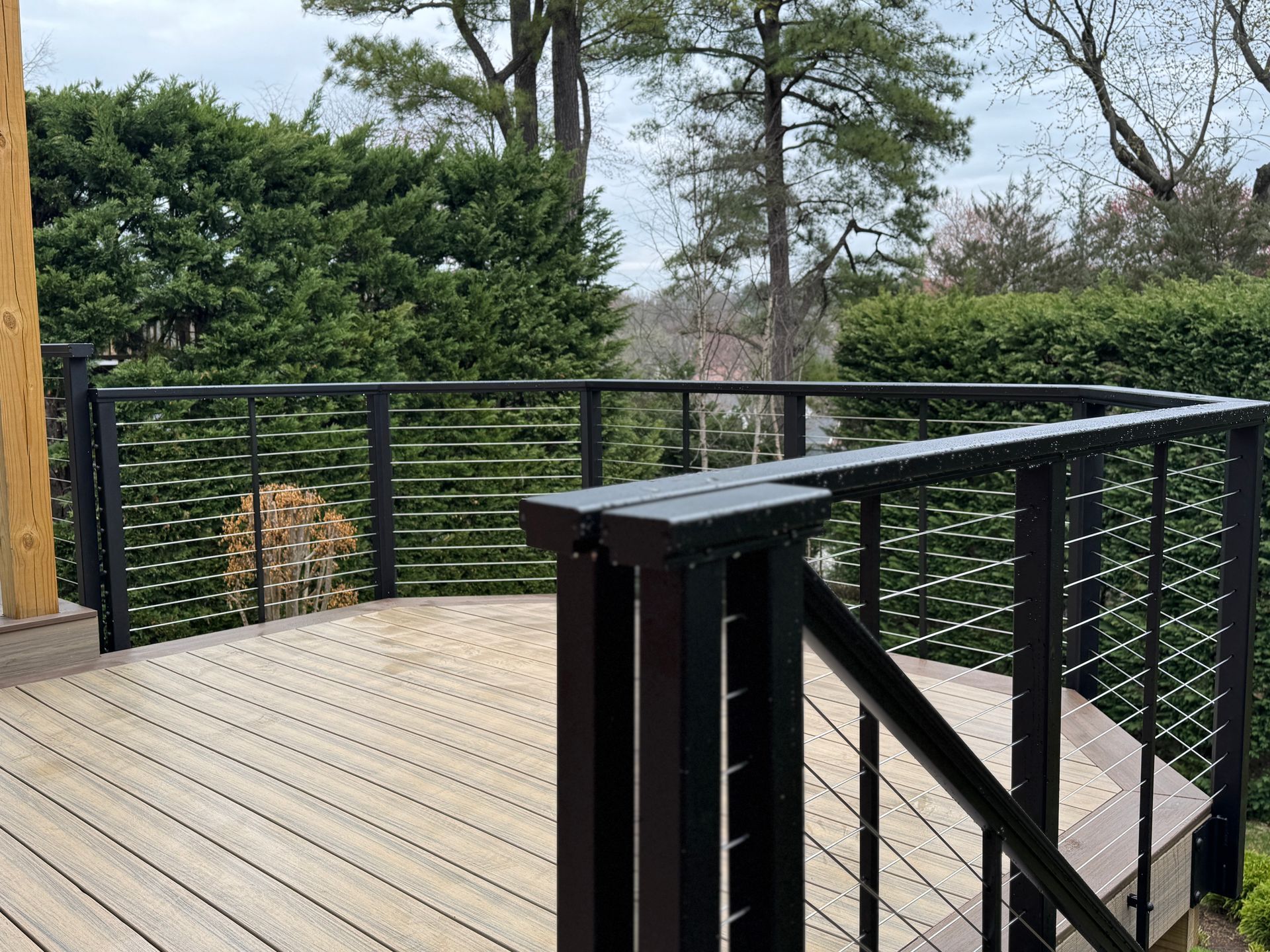 Wooden deck with black metal railing overlooking a green, tree-filled landscape.