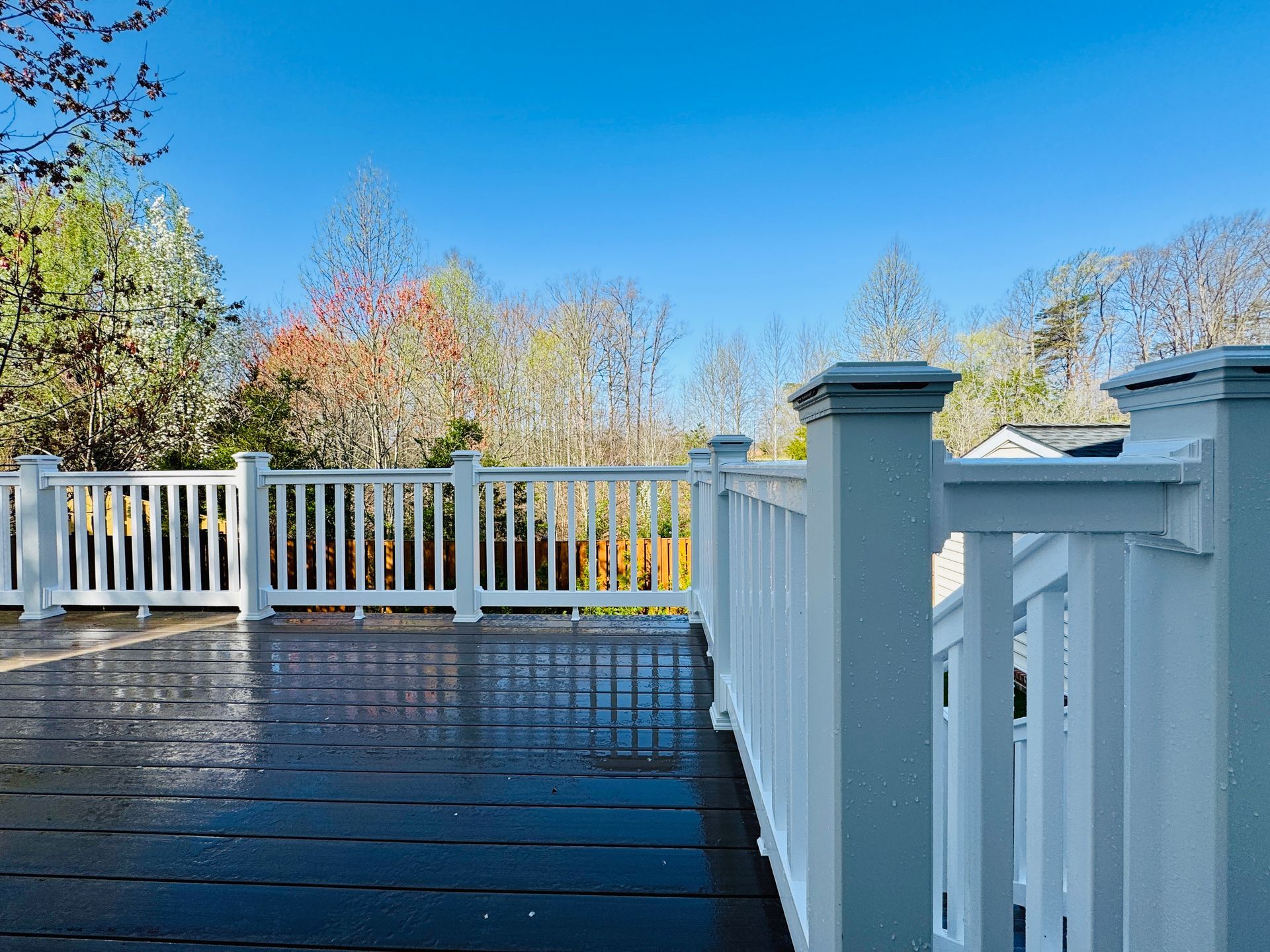 Wooden deck with white railing, overlooking trees and a clear blue sky.