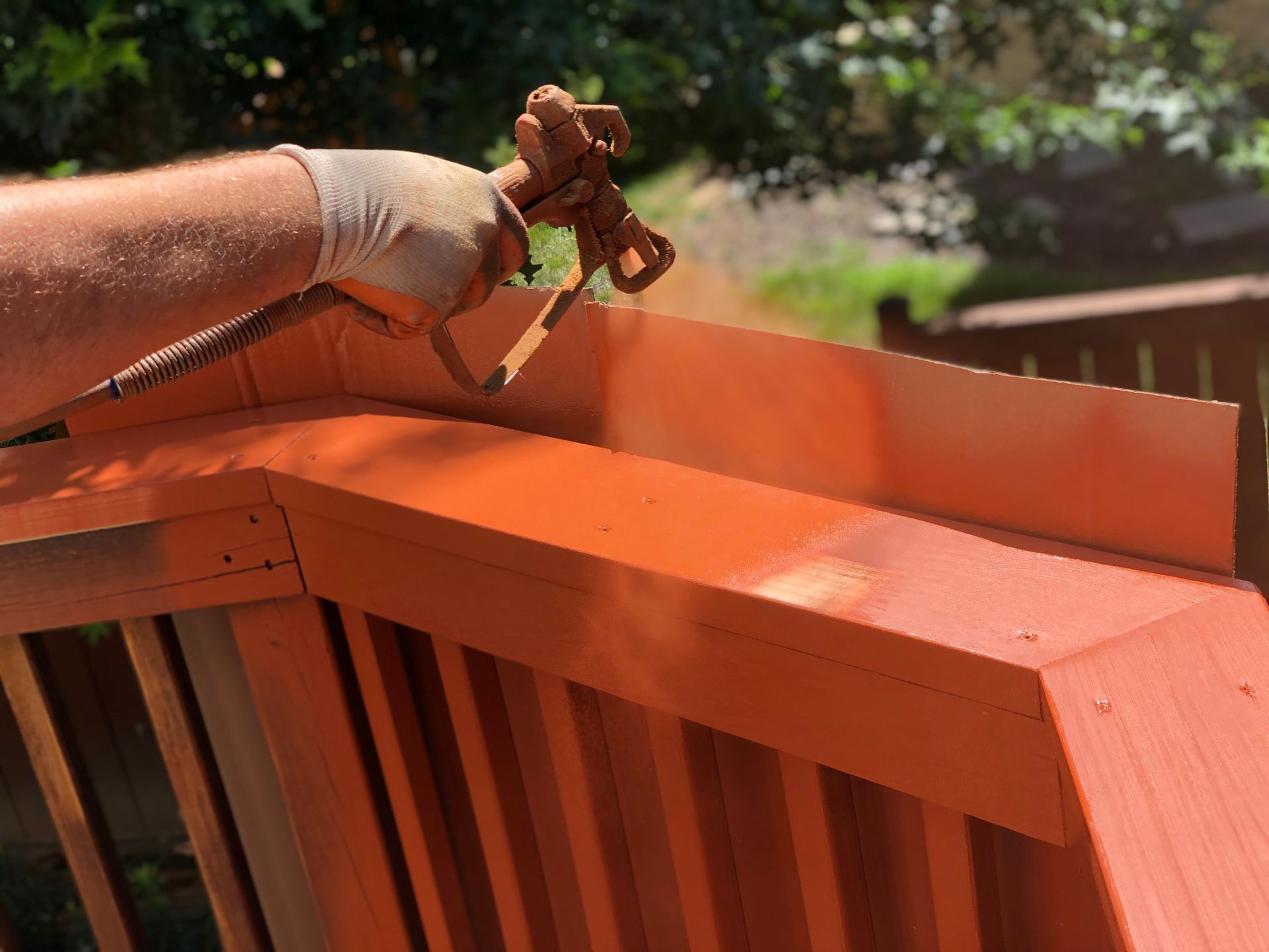 Person spray painting orange railing on a deck with an airless sprayer outside.