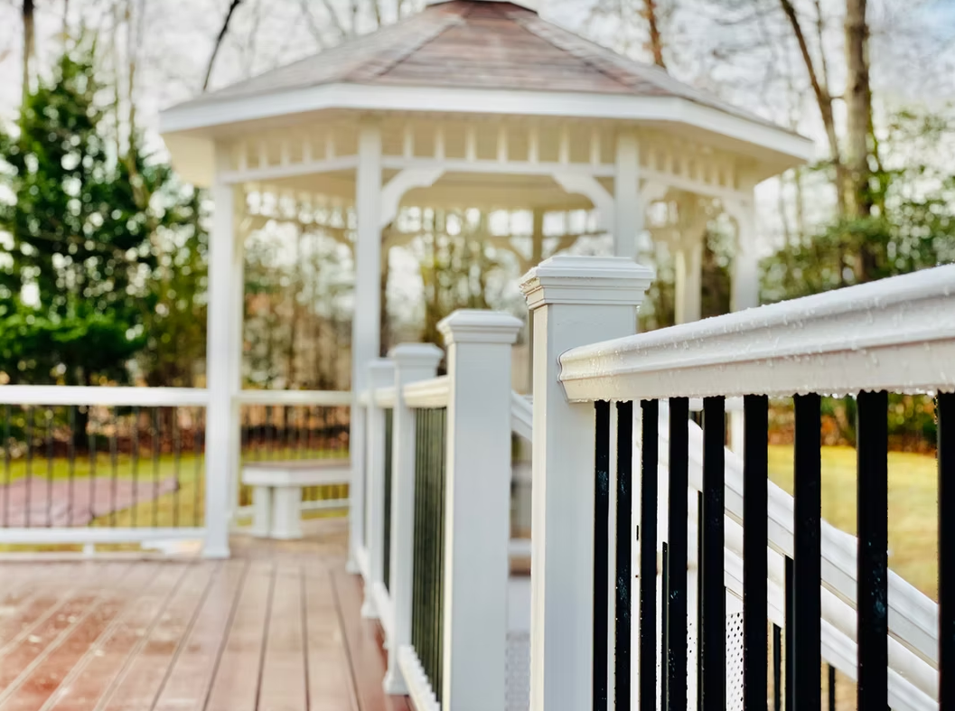 White gazebo on a wooden deck with black railing. Overcast, outdoor setting.