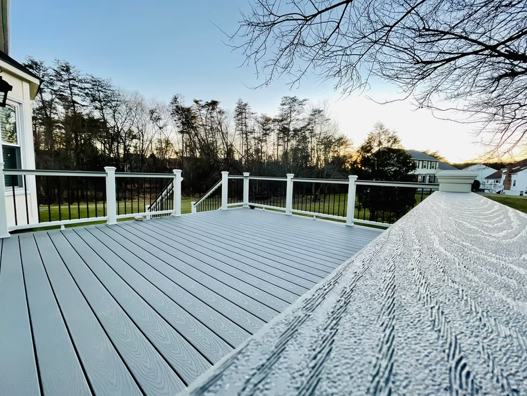 Gray wooden deck overlooking a yard and trees under a cloudy sky.