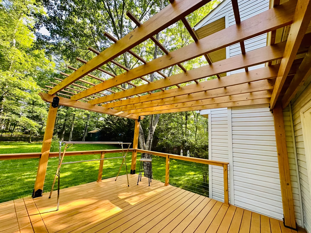 Wooden deck with pergola, overlooking a green lawn and trees.