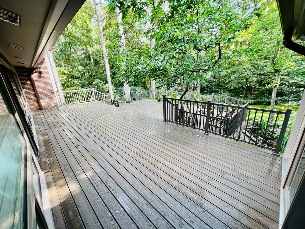 Wooden deck overlooking a wooded area with trees and outdoor furniture.