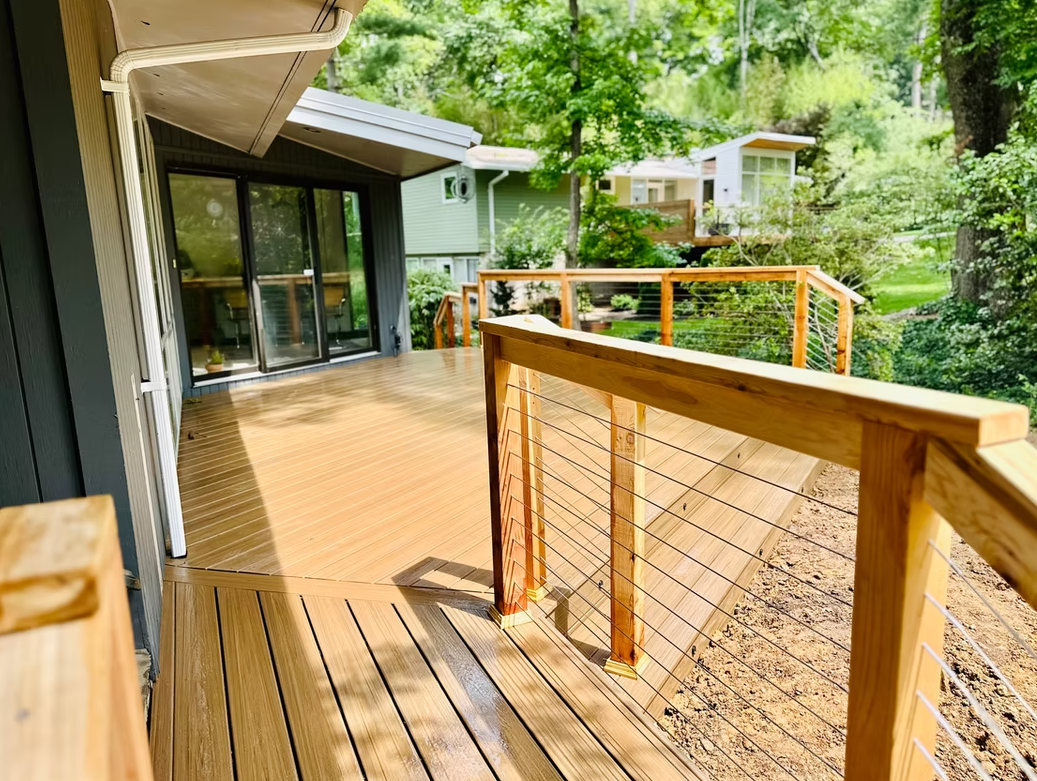 Wooden deck with cable railing overlooking a yard with a house.