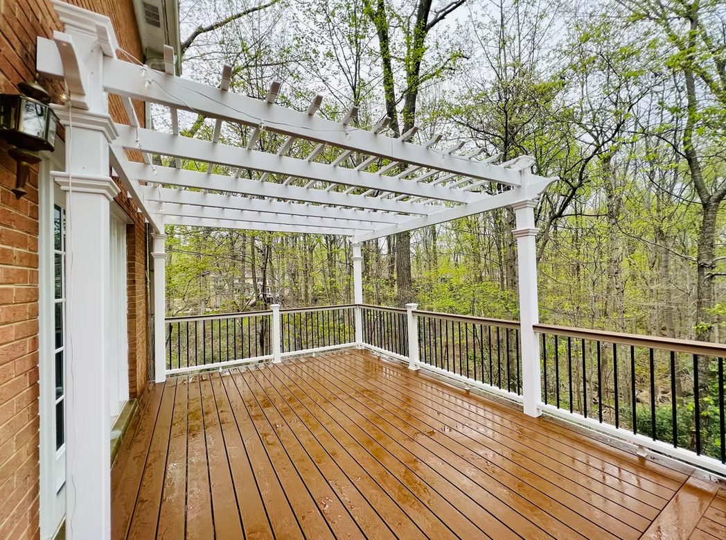 Wooden deck with white pergola, black railing, and surrounding trees.