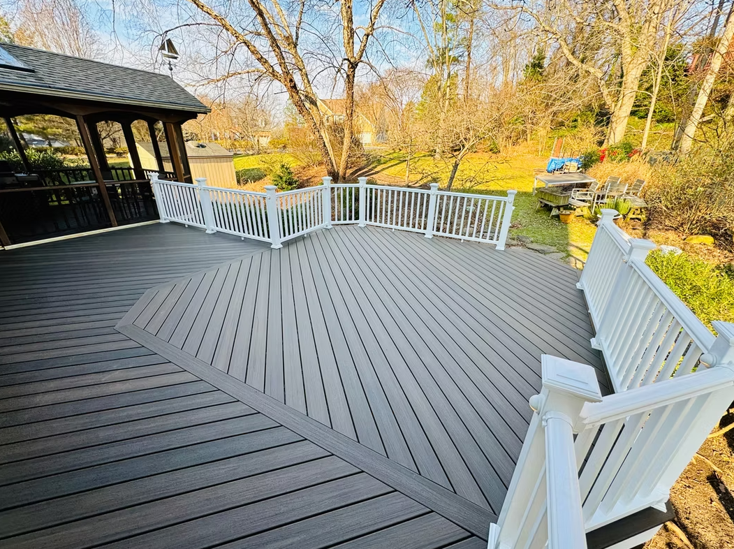 Elevated wooden deck with white railing, overlooking a wooded area. The deck's surface is gray.