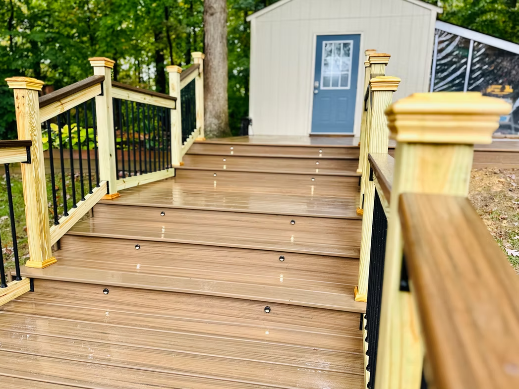 Wooden deck with steps leading to a shed with a blue door; black railings, tan wood.