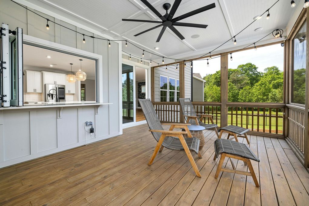 Screened-in porch with wood deck, seating, open window to kitchen, and string lights.
