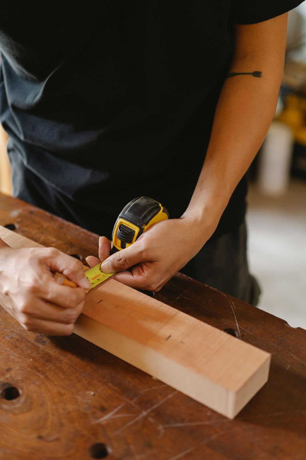 Person measuring and marking a wooden plank with a tape measure on a workbench.
