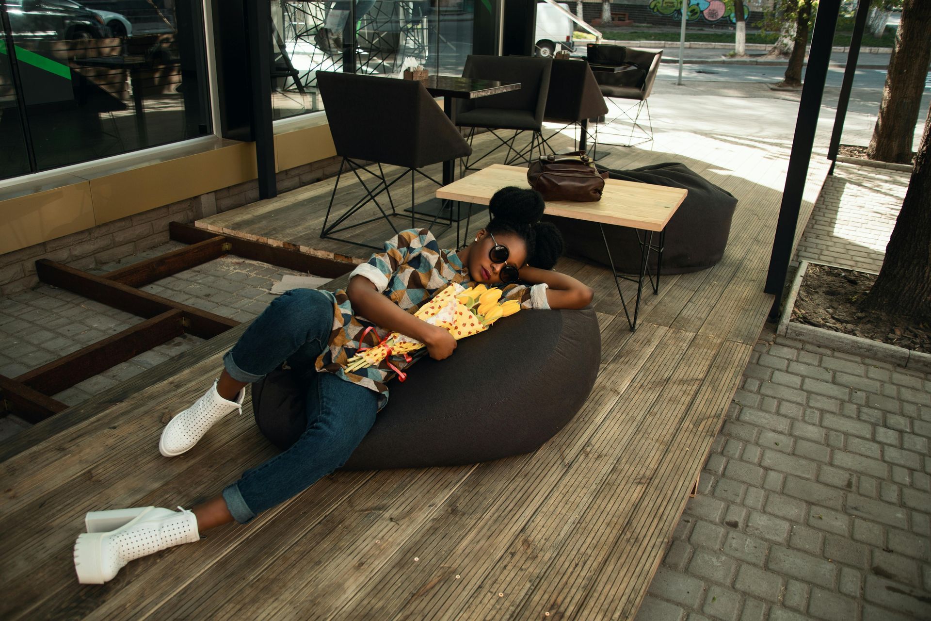 Woman reclining on a beanbag with popcorn, outdoors. Wearing jeans, shirt, sunglasses.