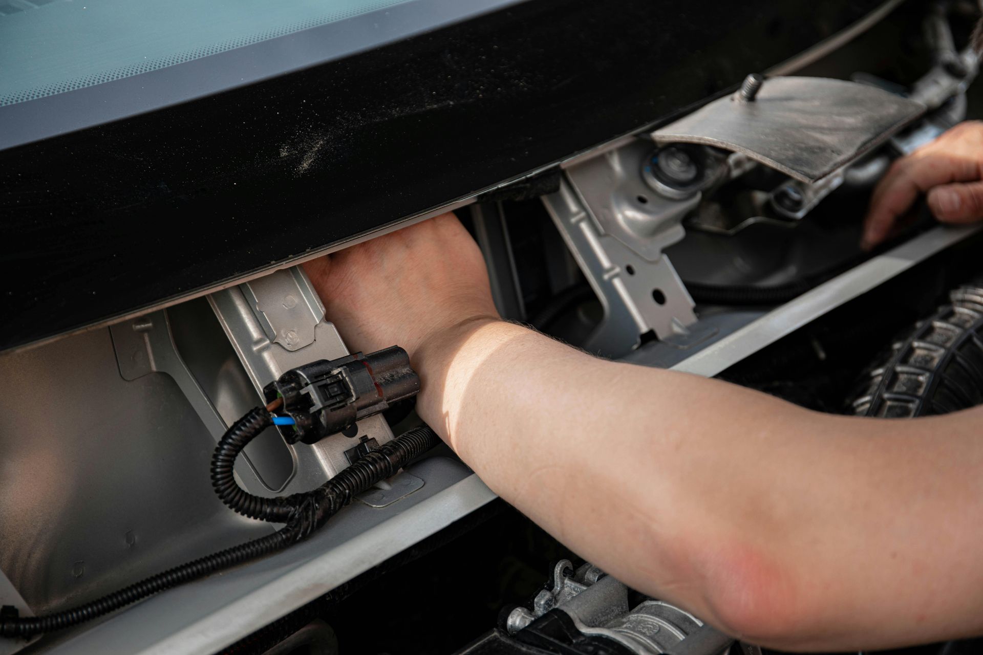 Person reaching into a car dashboard compartment with wiring exposed
