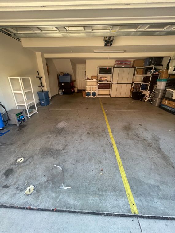 An empty, concrete-floored residential garage with storage shelves along the back wall and a yellow line painted on the floor.