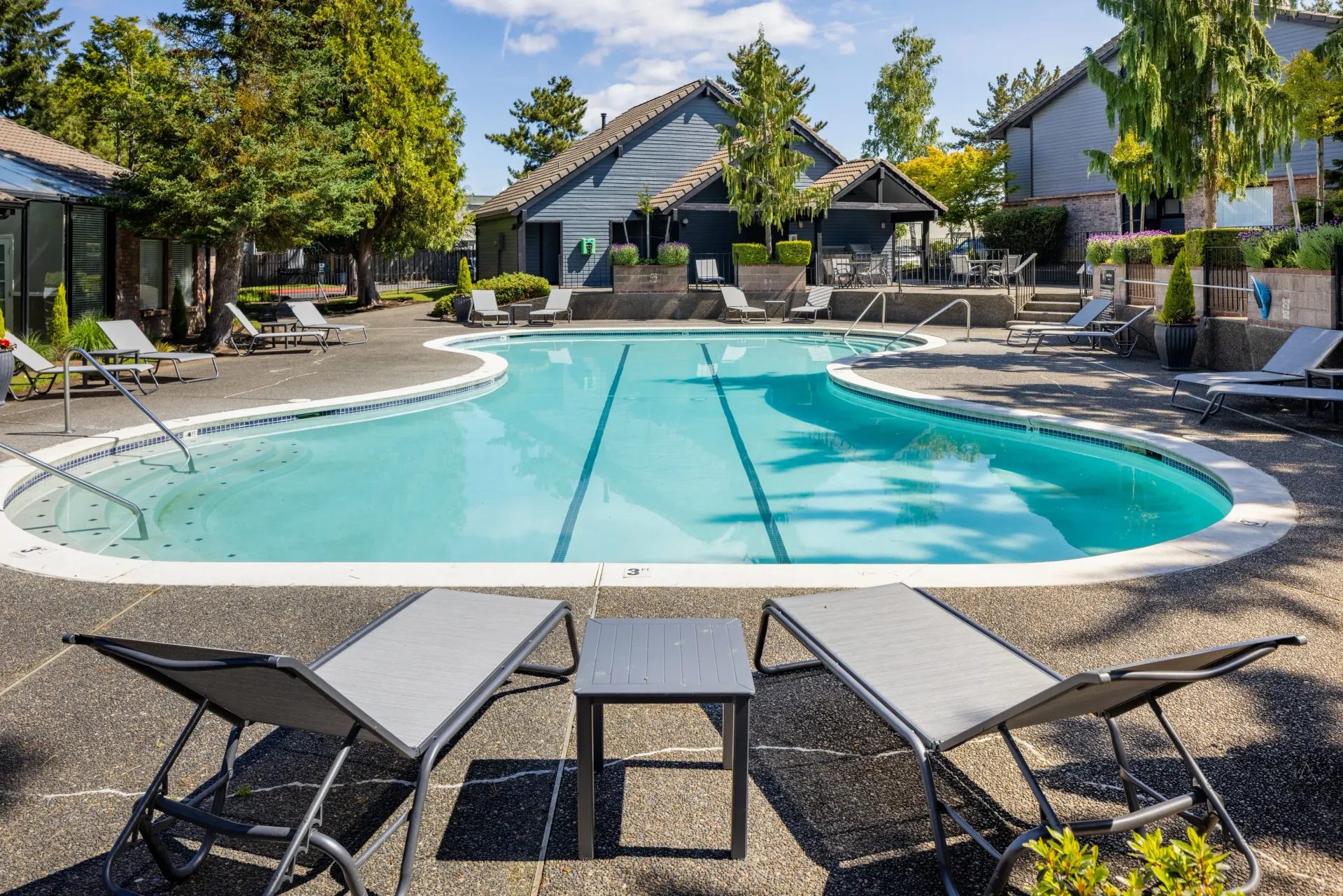 Outdoor community pool with lounge chairs and tables, surrounded by trees at Ansley Murrayhill in Tigard, OR.