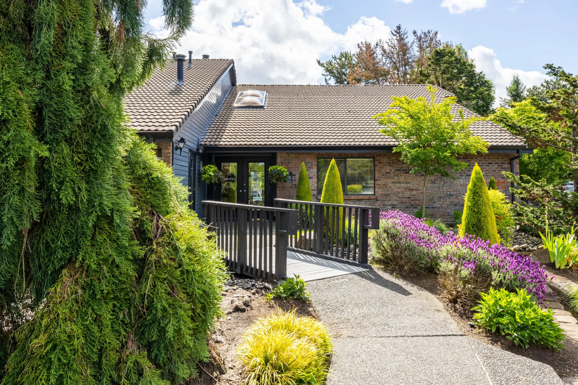 Exterior entrance of an apartment building with a wooden ramp and landscaped garden at Ansley Murrayhill in Tigard, OR.