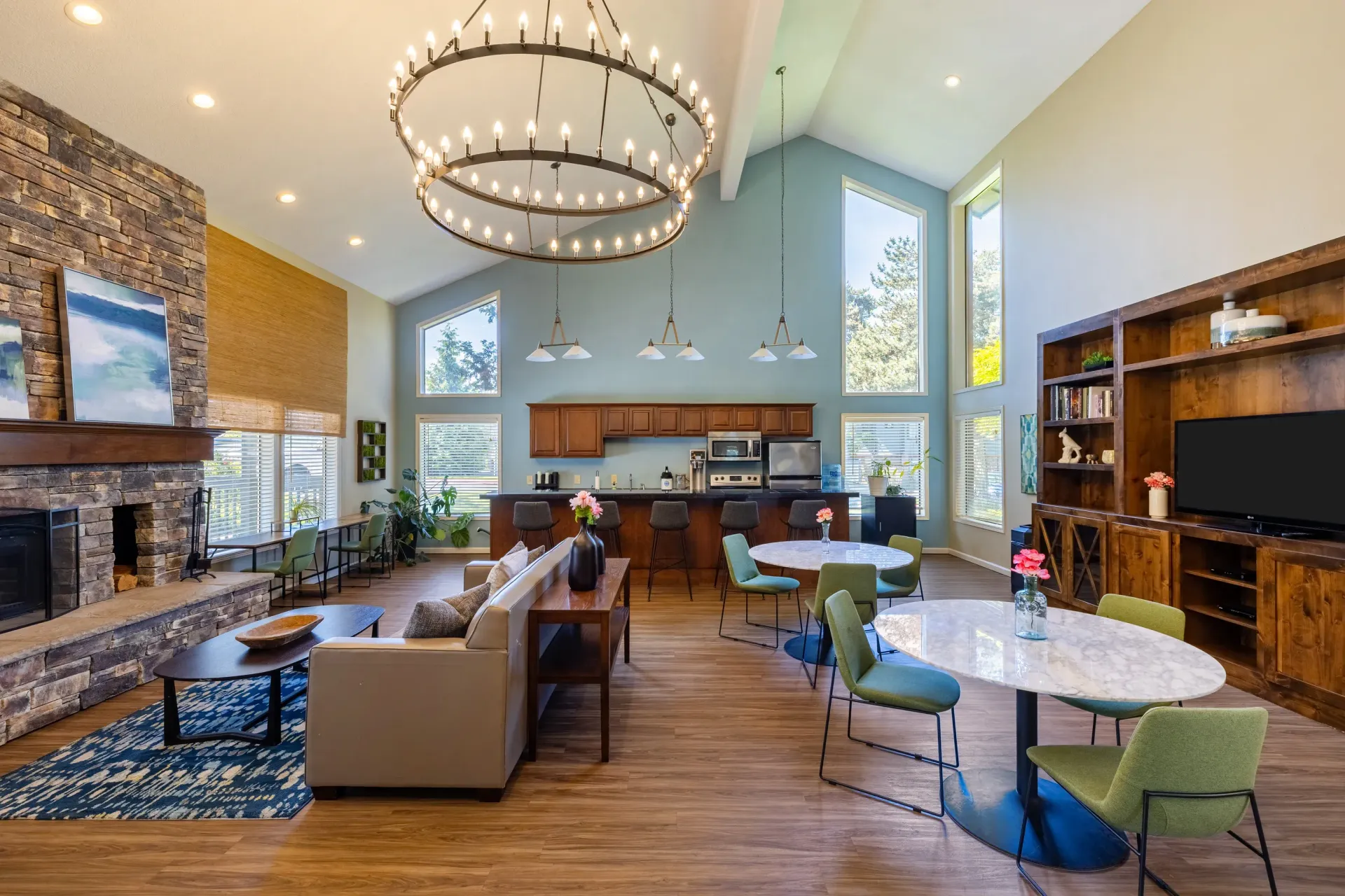 Open communal living space with a stone fireplace, kitchen, and round chandeliers at Ansley Murrayhill in Tigard, OR.