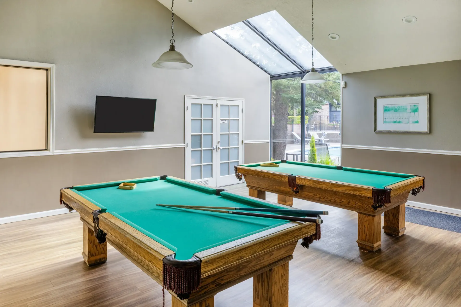 Communal game room with two pool tables, a wall-mounted TV, and a skylight at Ansley Murrayhill in Tigard, OR.