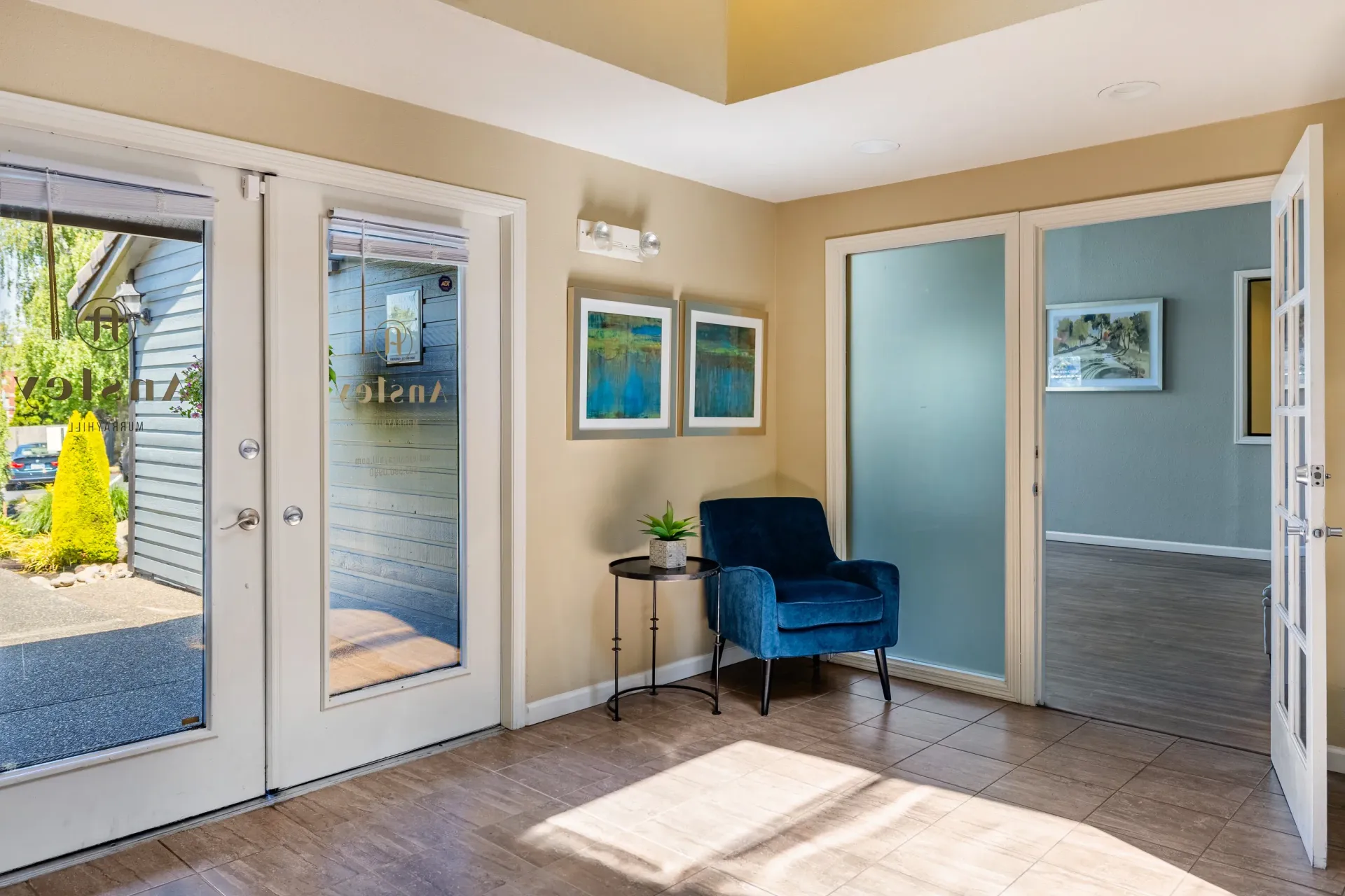 Lobby area with glass entry doors, a blue chair, and frosted glass doorway at Ansley Murrayhill in Tigard, OR.