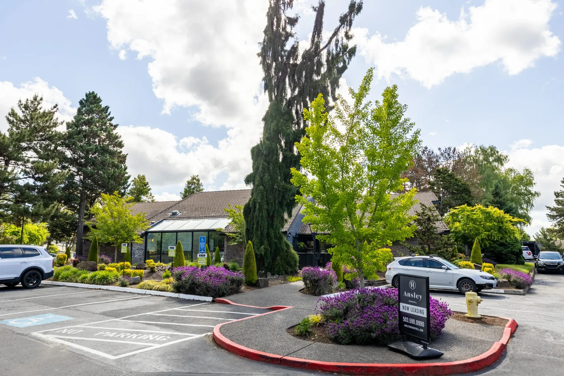 Exterior view of a multifamily property with landscaped entry, signage, and parking area at Ansley Murrayhill in Tigard, OR.