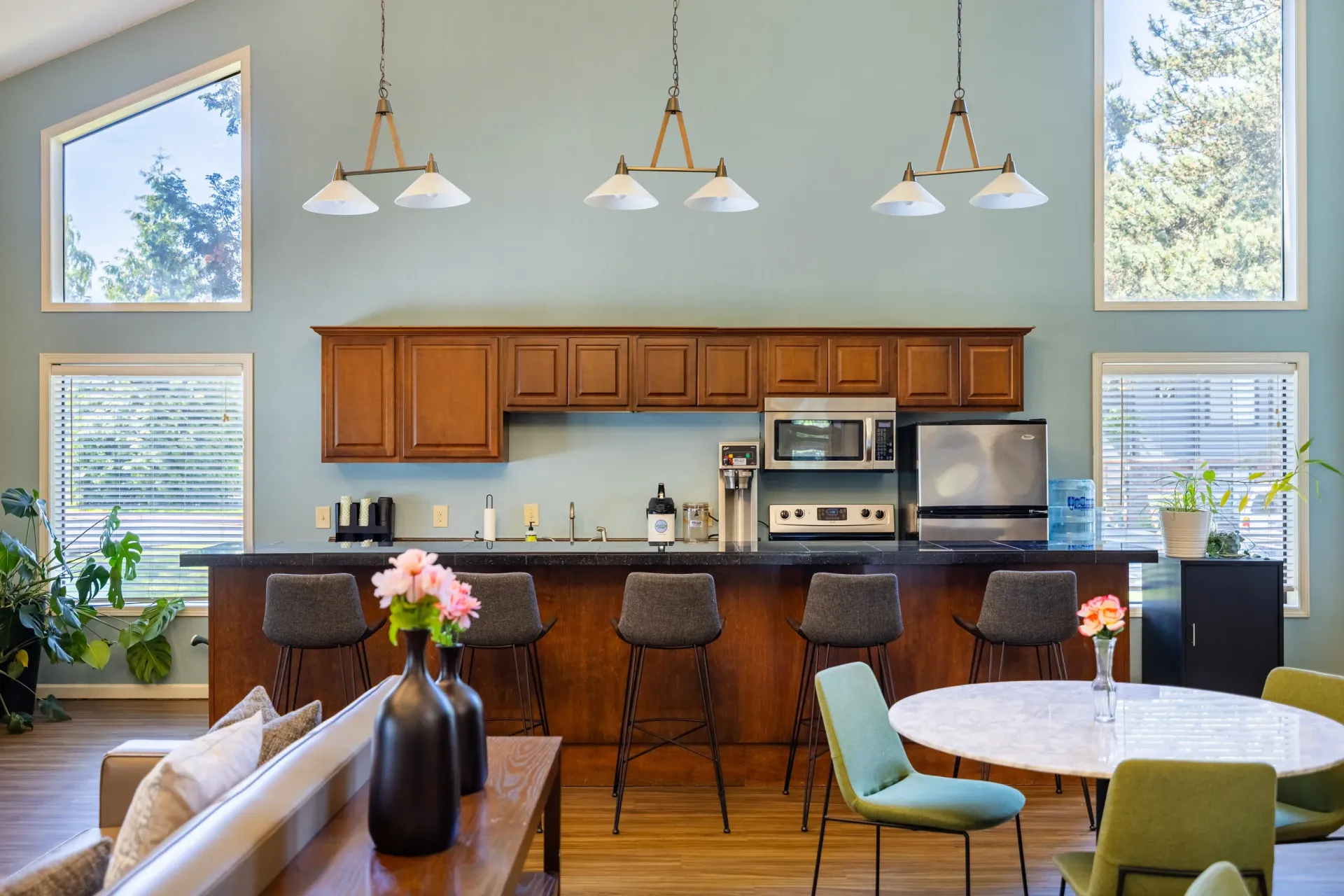 Bright communal kitchen with a long counter, wooden cabinets, pendant lights, and a round table at Ansley Murrayhill in Tigard, OR.