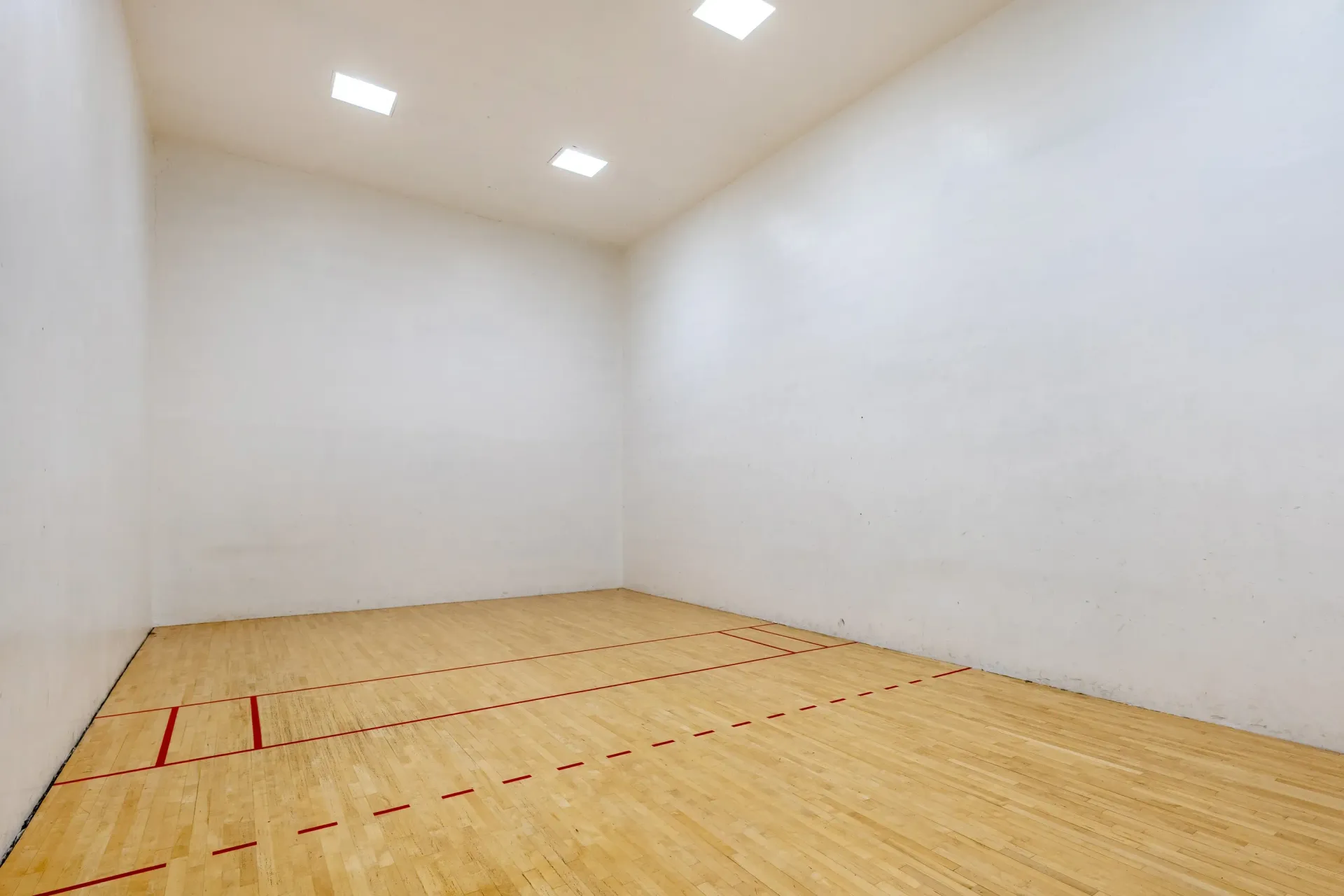 Empty indoor recreation space with a hardwood sport court, red lines, white walls and bright ceiling lights at Ansley Murrayhill in Tigard, OR.