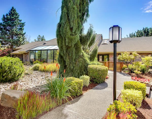 Exterior of apartment community with a paved walkway, tall tree, and landscaped shrubs at Ansley Murrayhill in Tigard, OR.