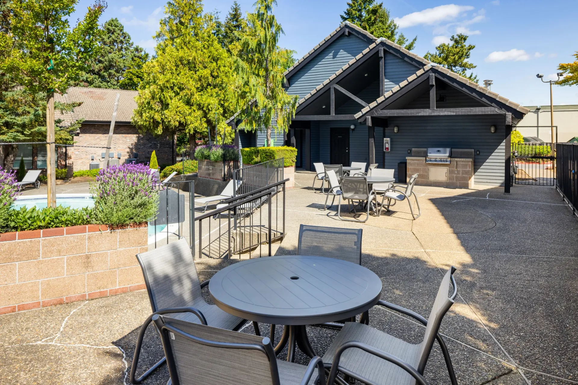 Outdoor community patio with tables, chairs, a grill station, and landscaping beside the pool at Ansley Murrayhill in Tigard, OR.