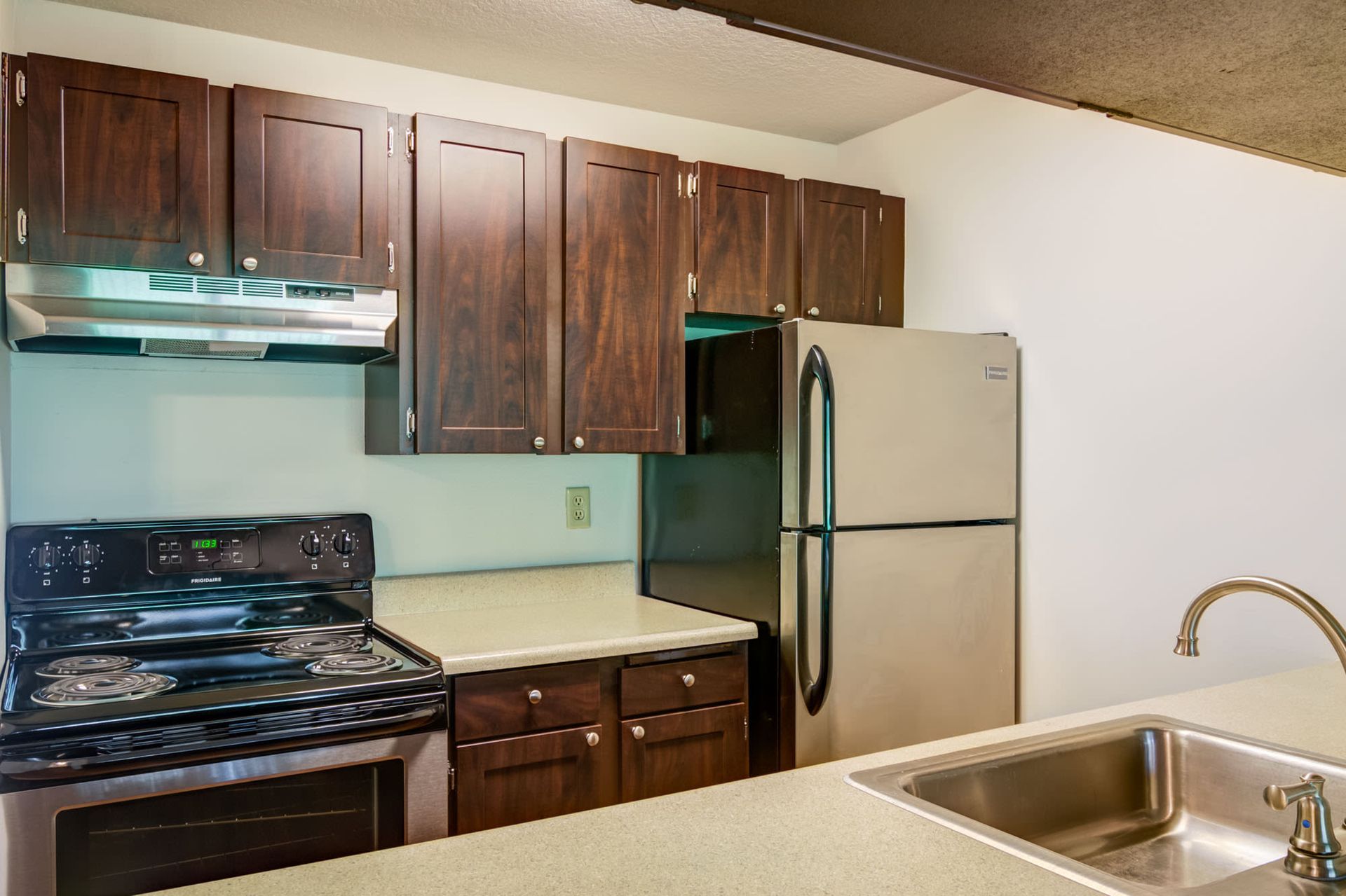 Kitchen with dark wood cabinets, stainless steel fridge, stove, and sink at Ansley Murrayhill in Tigard, OR.