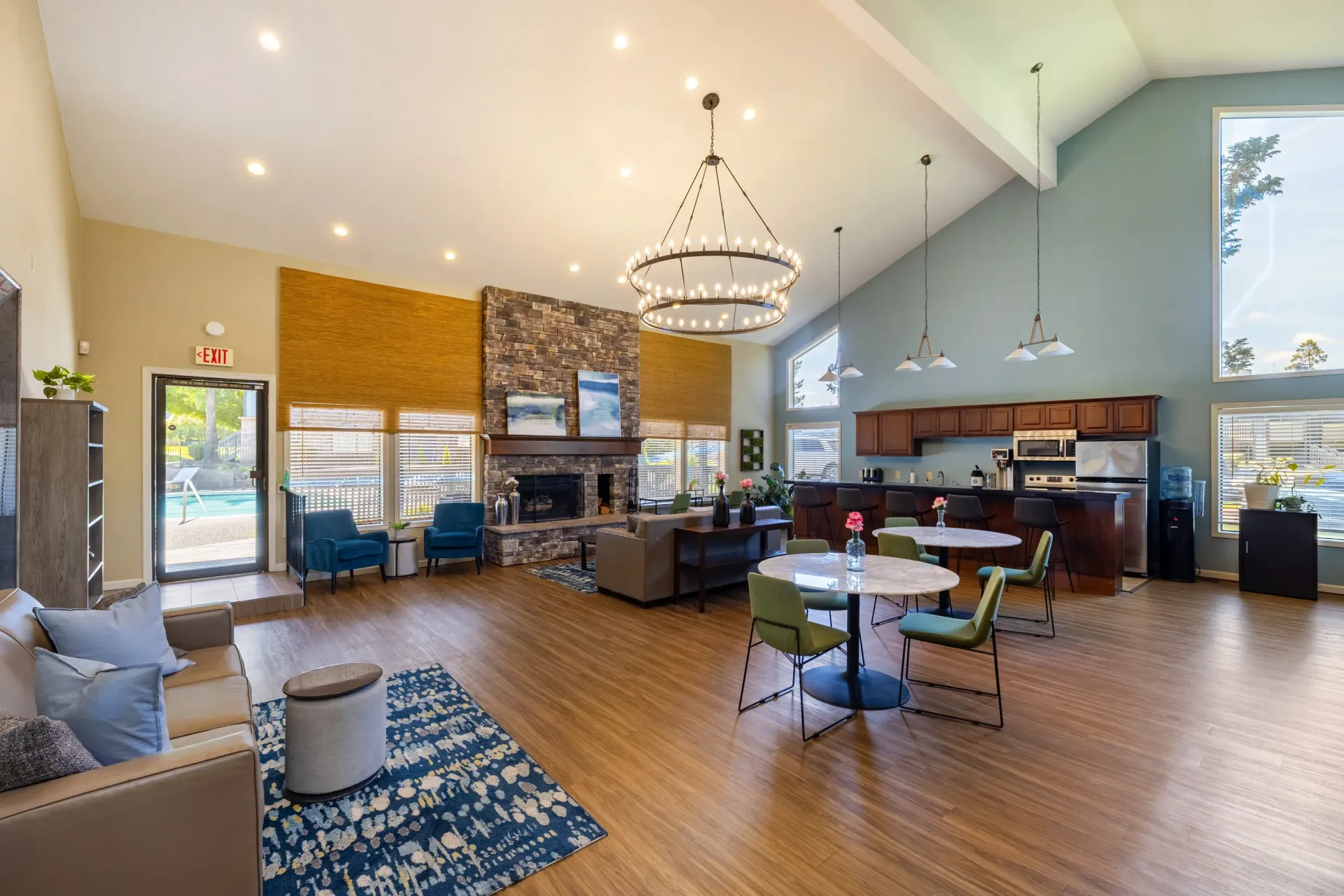 Bright resident lounge with a stone fireplace, vaulted ceiling, large windows, and a full kitchen at Ansley Murrayhill in Tigard, OR.
