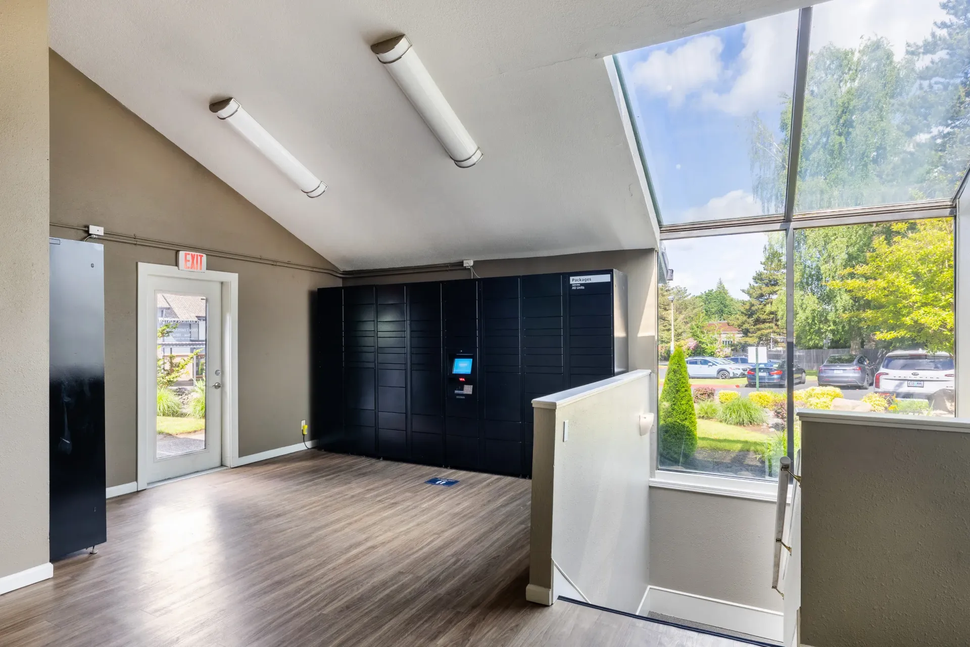 Interior of a community package locker area with dark lockers and a large window at Ansley Murrayhill in Tigard, OR.