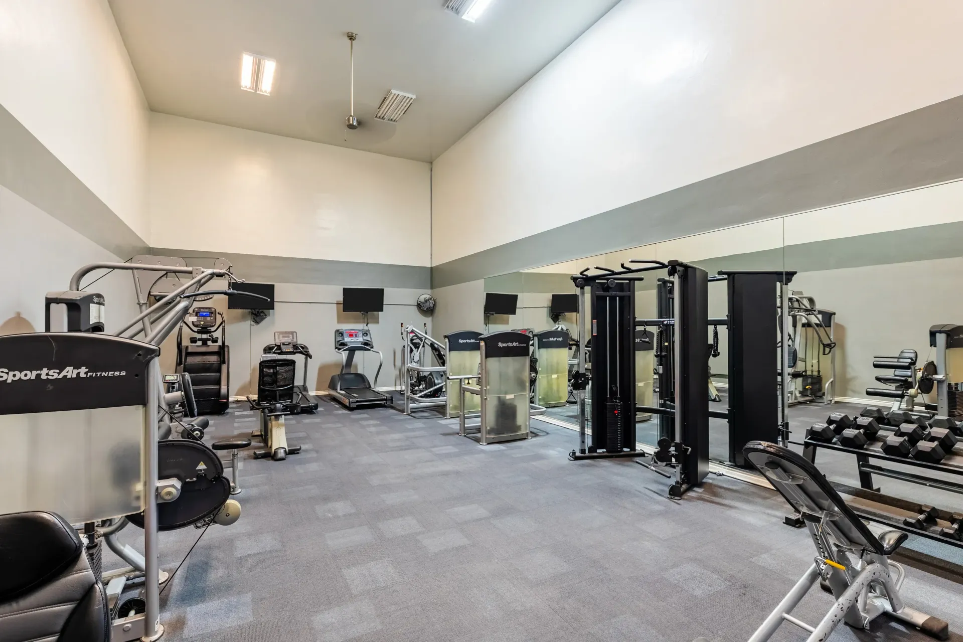Indoor community gym with cardio machines, weight machines, and a mirrored wall at Ansley Murrayhill in Tigard, OR.