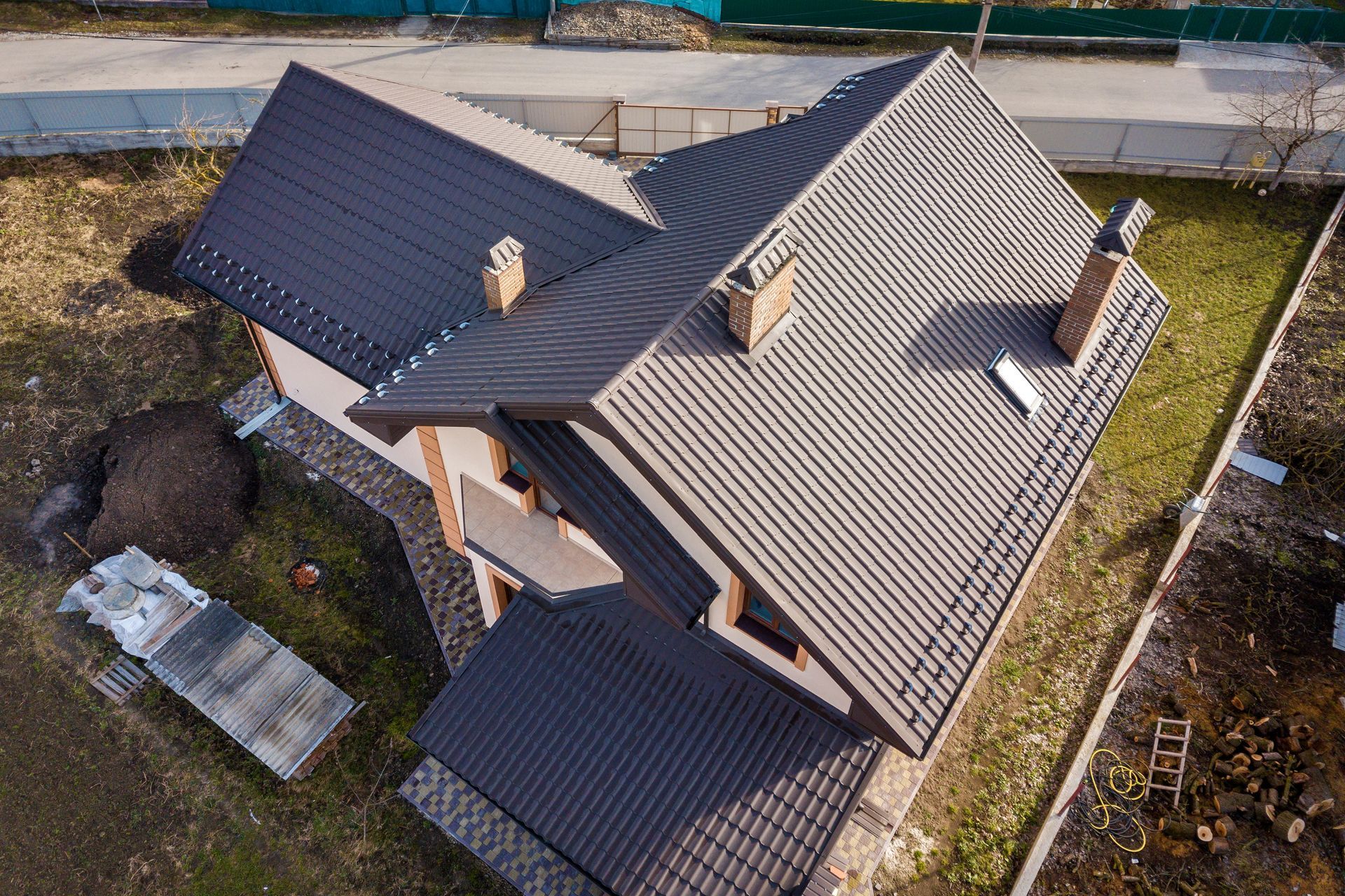 Aerial view of a house with a dark gray, multi-sloped roof. Chimneys and a small yard are visible.