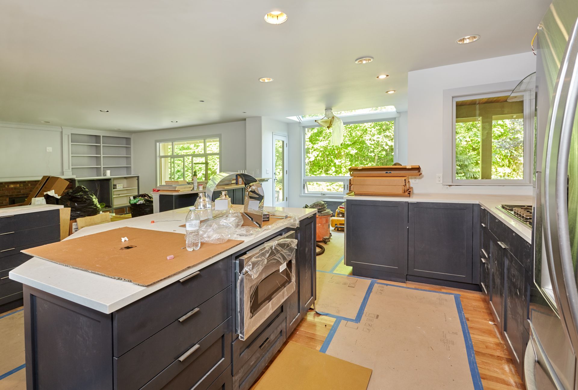 Kitchen under renovation with blue cabinets, stainless steel appliances, and cardboard covering the floor and countertops.