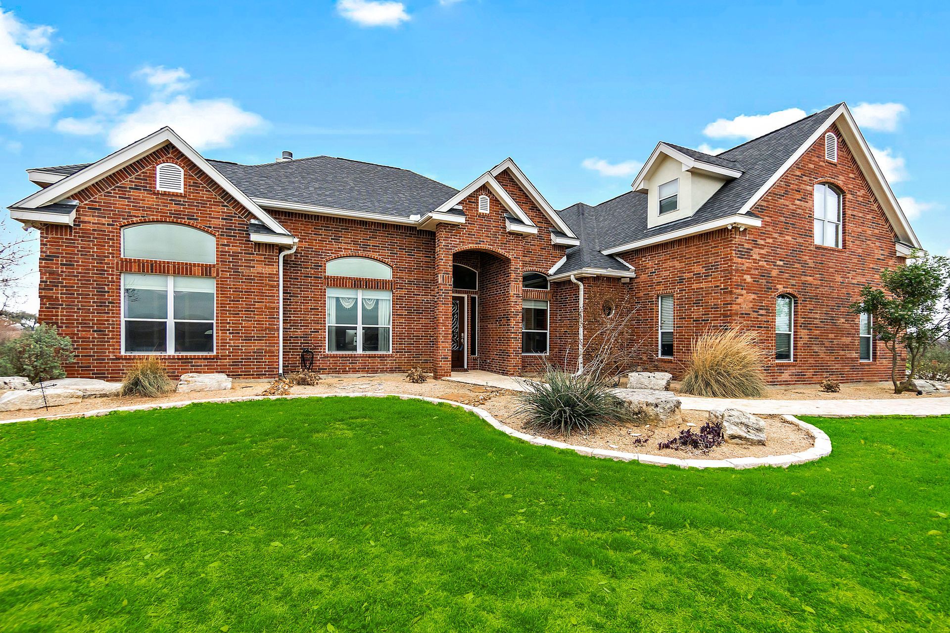 Brick house with a green lawn under a blue sky.