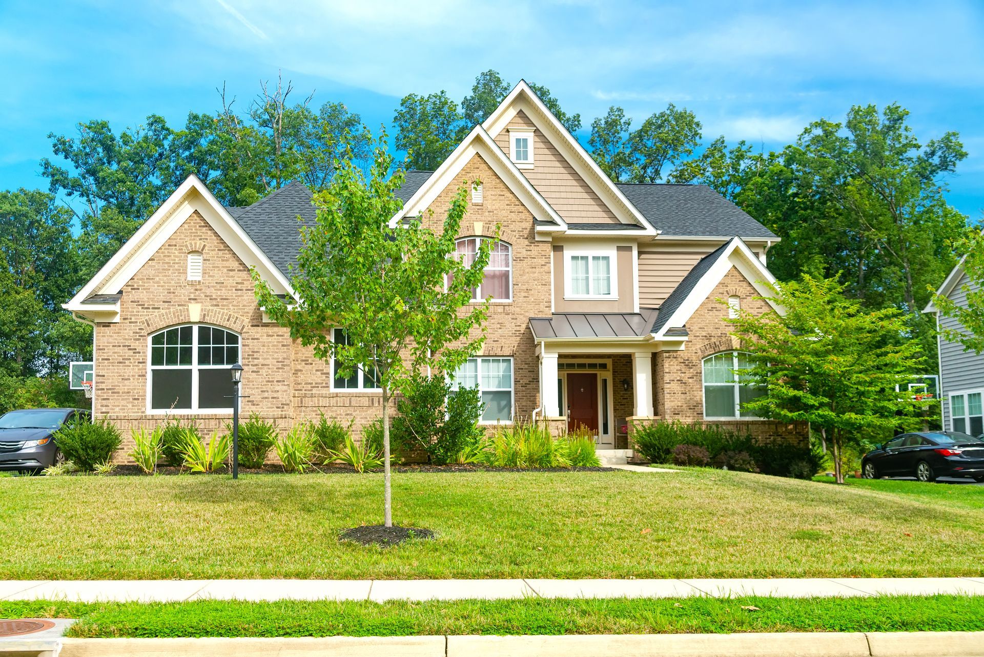 Two-story brick house with a green lawn and trees under a bright blue sky.