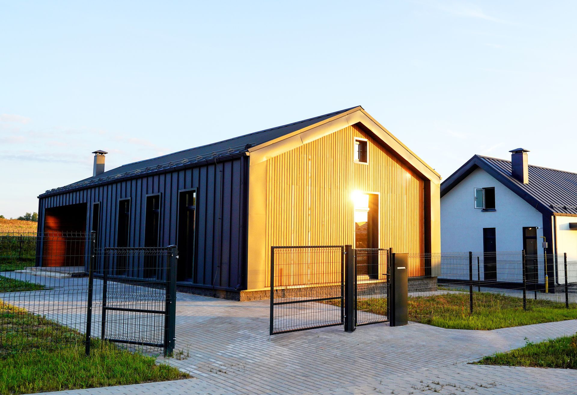 Modern wooden house with metal roof, set against a blue sky, sun shining in window.