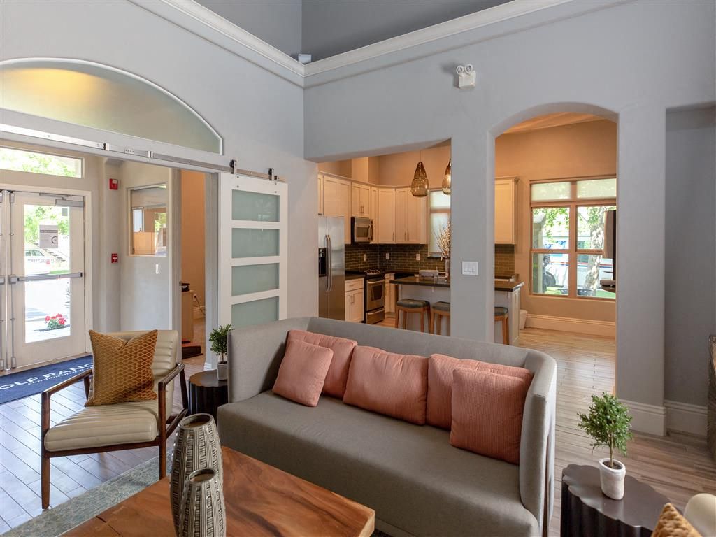 Open-concept living area with a gray sofa, pink cushions, and a view into the kitchen.